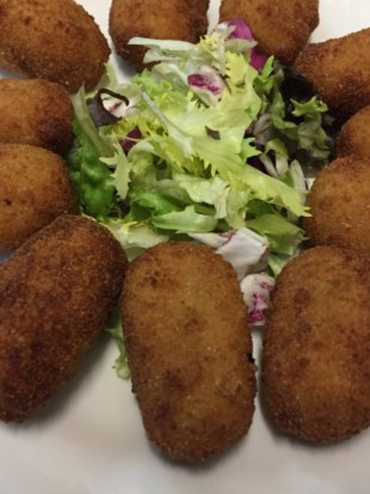 Before: dark phone photo of croquetas and patatas bravas on a wooden bar top in dim evening light