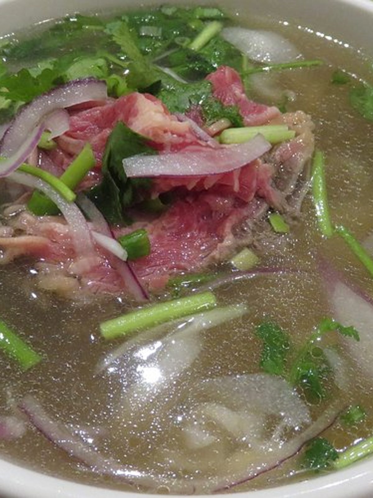 Before: dim phone photo of a bowl of pho with beef and herbs on a kitchen counter under flat light