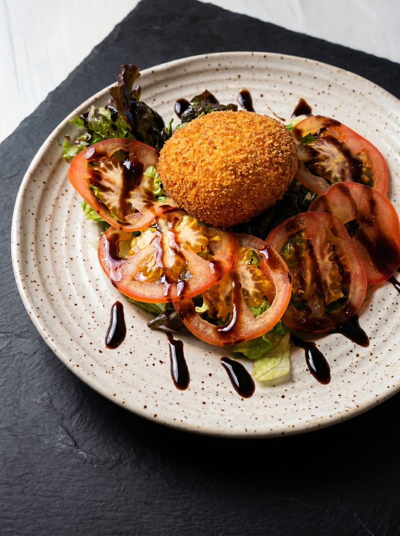 After: studio-lit menu photo of the same cut-open scotch egg with golden crumb and rich yolk clearly visible
