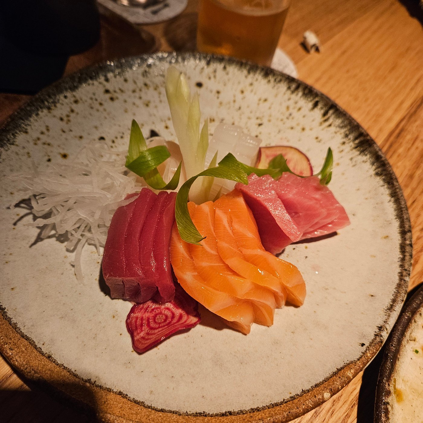Phone photo of a sushi platter under flash, fish showing a harsh white hotspot and rice looking like a pale lump